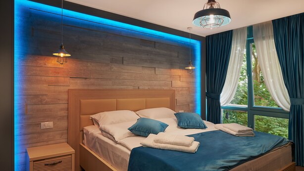 A modern bedroom with a wooden headboard, a large bed with blue bedding, and a nightstand with drawers. - Piata Unirii Central Apartments (Iasi)