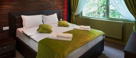 A neatly made bed with green and white bedding, a brick accent wall, and a window with sheer curtains.