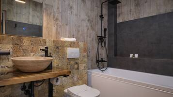 A modern bathroom with a stone sink, a toilet, and a bathtub.