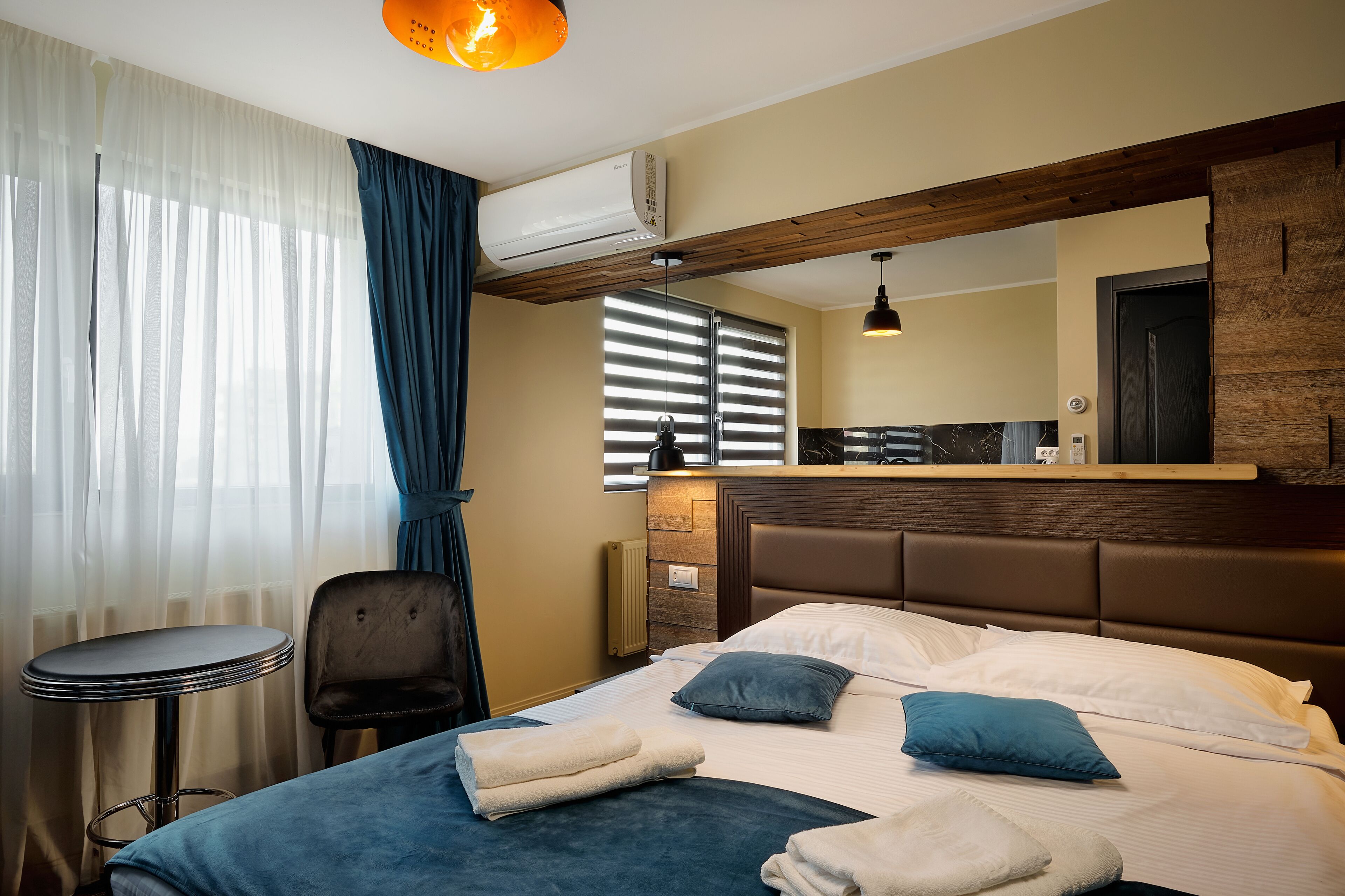 A hotel room with a bed, a chair, a small table, and a window with blinds.