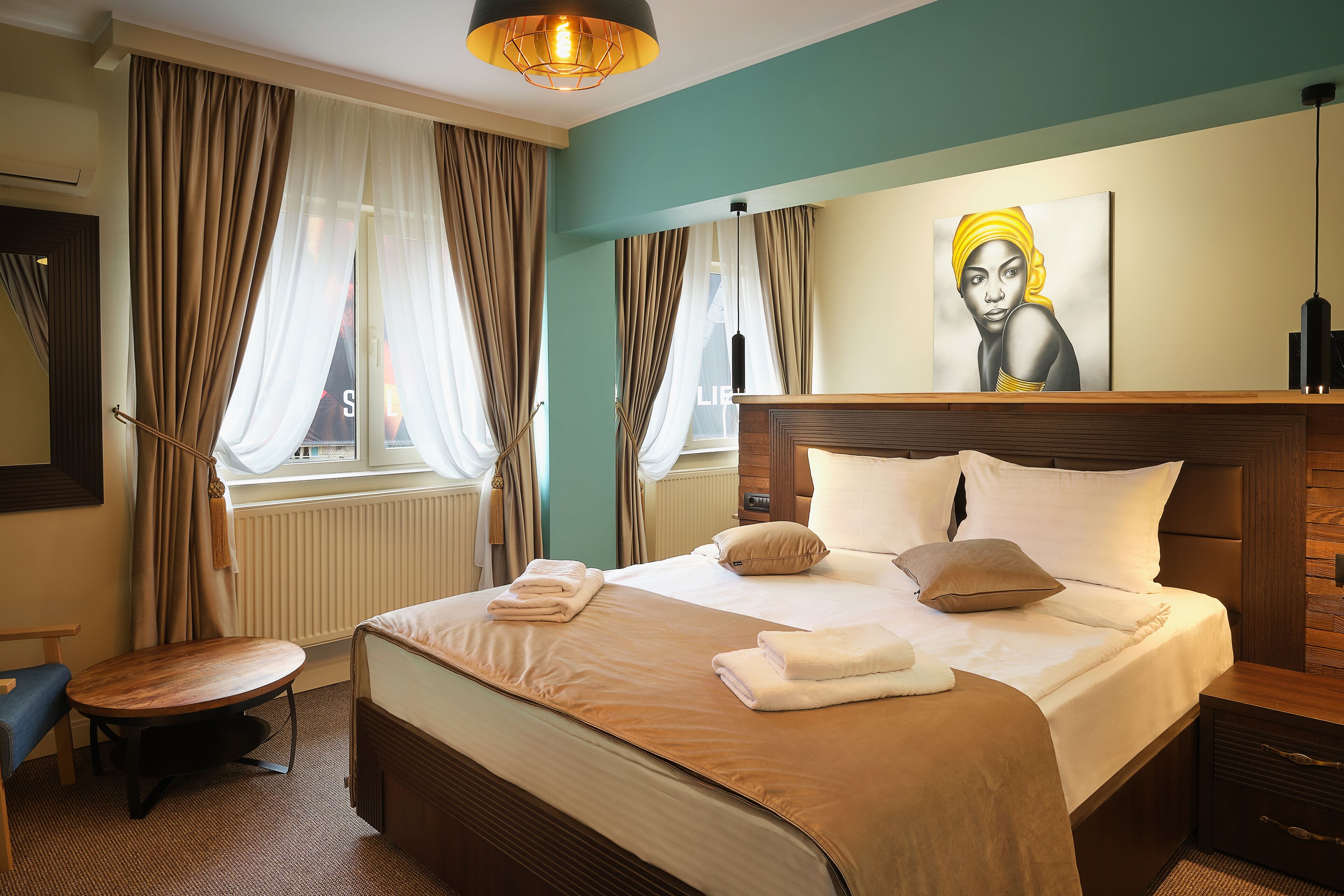 A hotel room with a large bed, a wooden headboard, a round table, and a painting on the wall.