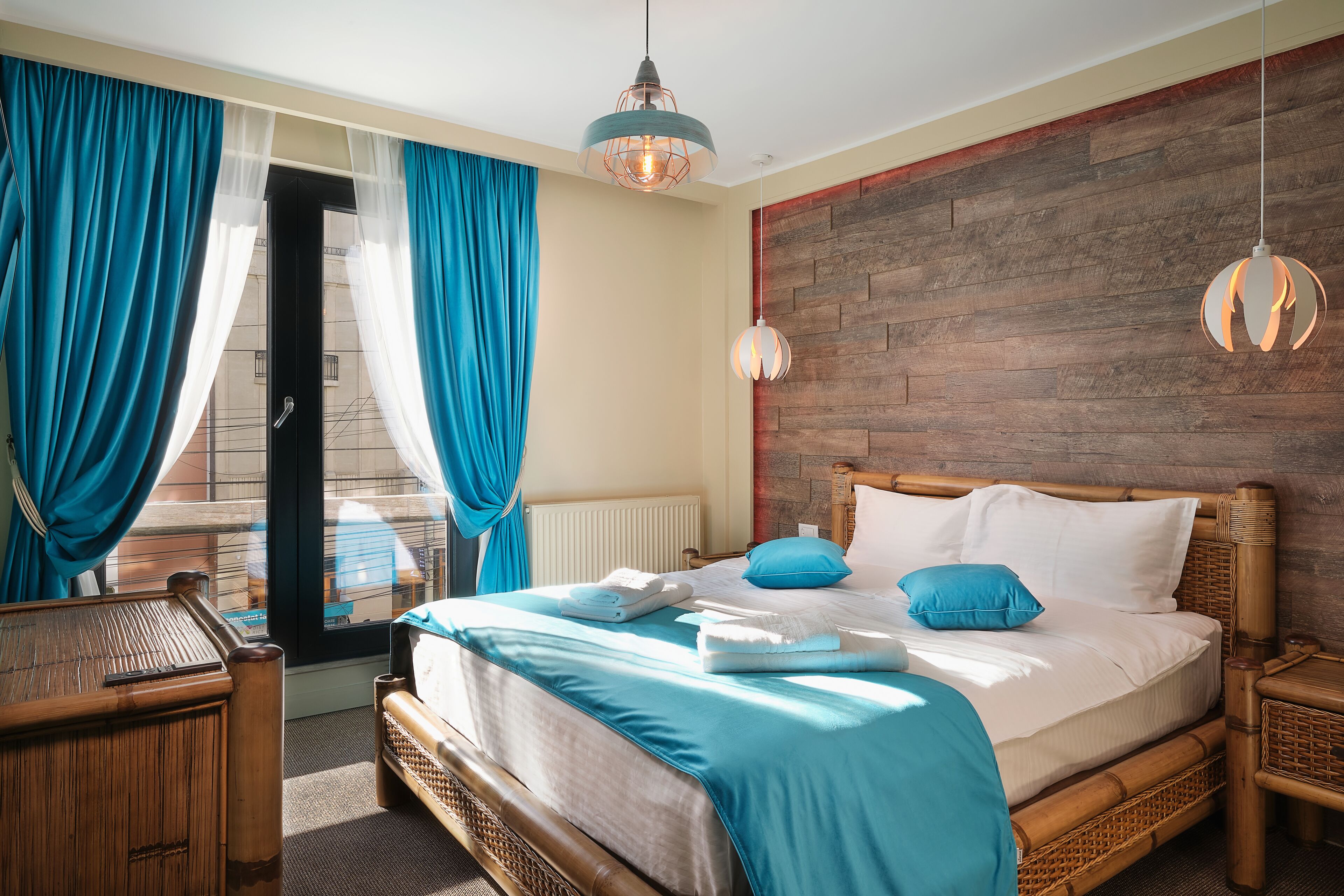 A well-lit bedroom with a large bed, blue curtains, and a wooden headboard.