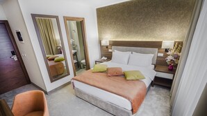 A hotel room with a large bed, a chair, a mirror, a nightstand with a lamp, and a bathroom visible through a door. - Hotel Marshal (Belgrade)
