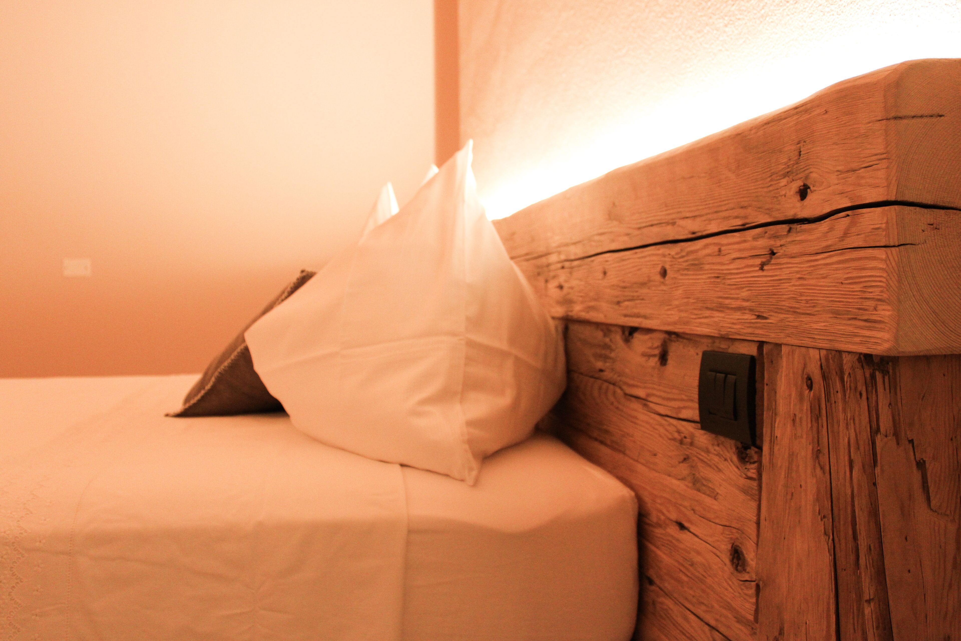 A wooden headboard with a switch, a white pillow, and a folded blanket on a bed.