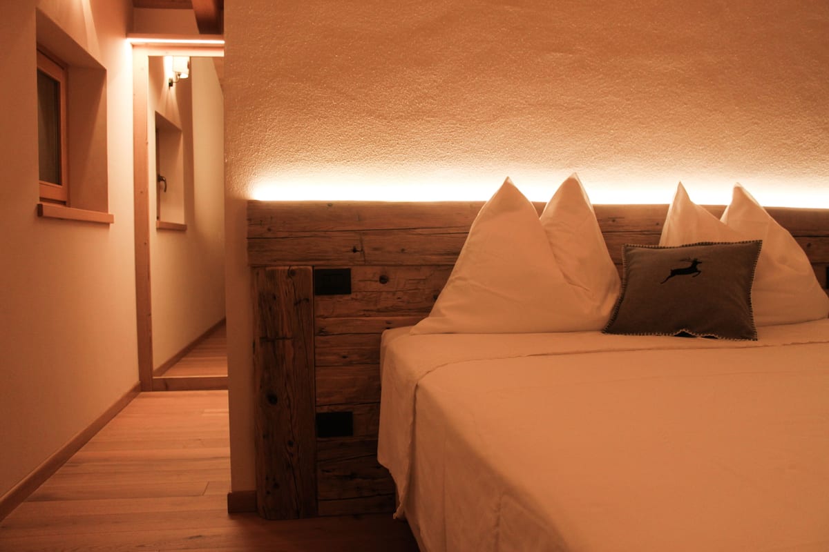 Une chambre à coucher avec une tête de lit en bois, un lit avec une literie blanche et un oreiller orné d’un logo.
