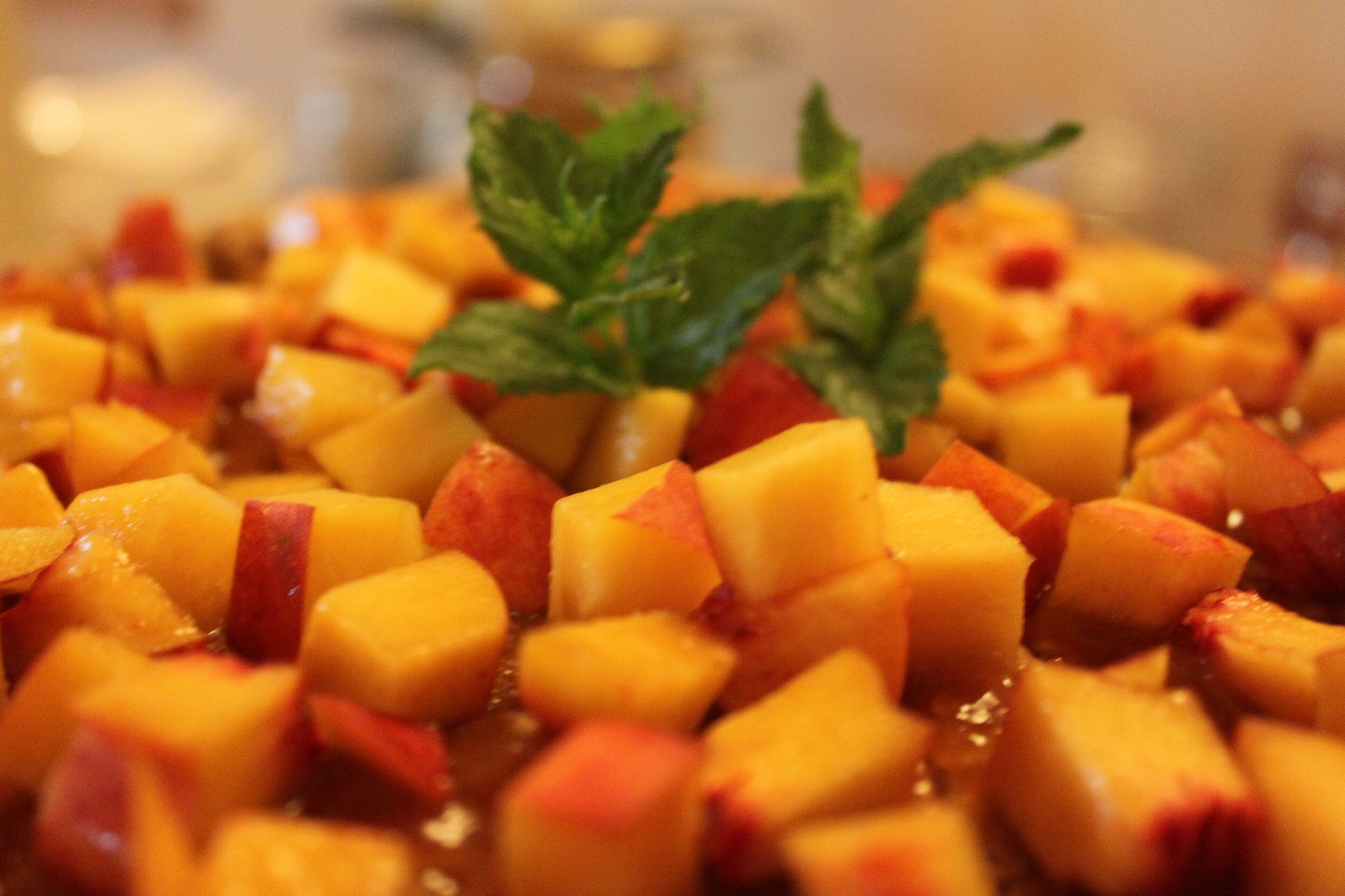 A close-up of diced fruit, possibly peaches or mangoes, with a garnish of mint leaves.
