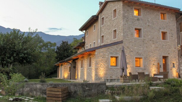 Un bâtiment en pierre doté de nombreuses fenêtres et d’un patio aménagé avec du mobilier d’extérieur.