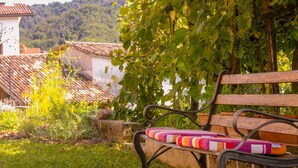 Un banc agrémenté d’un coussin coloré, situé dans un jardin, d’où l’on peut admirer des bâtiments et des collines en arrière-plan.