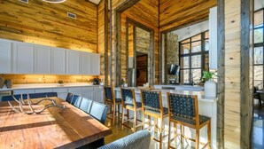 Eine Küche mit Holzwandverkleidung und weißen Schränken, ein Essbereich mit Holztisch und -stühlen sowie eine Steinwand mit einem Fernseher.