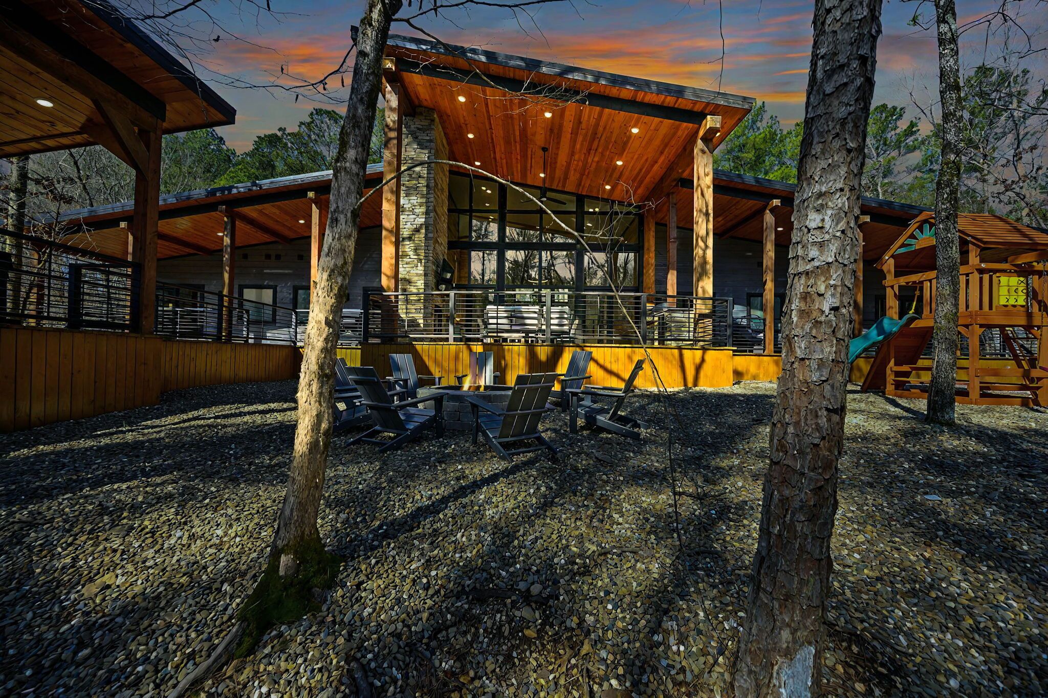 A modern building with a covered patio area, stone walls, and a wooden deck with a slide.