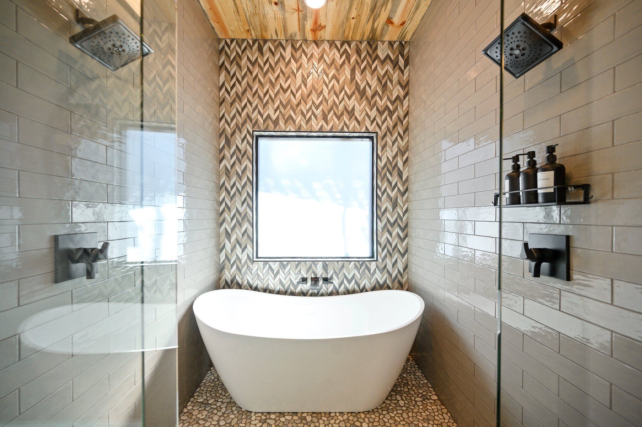 Ein modernes Badezimmer mit freistehender Badewanne, großem Fenster und einer Wand mit Fischgrätmuster.
