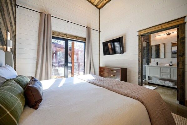 A bedroom with a large bed, a dresser, a mirror, and a window with curtains.