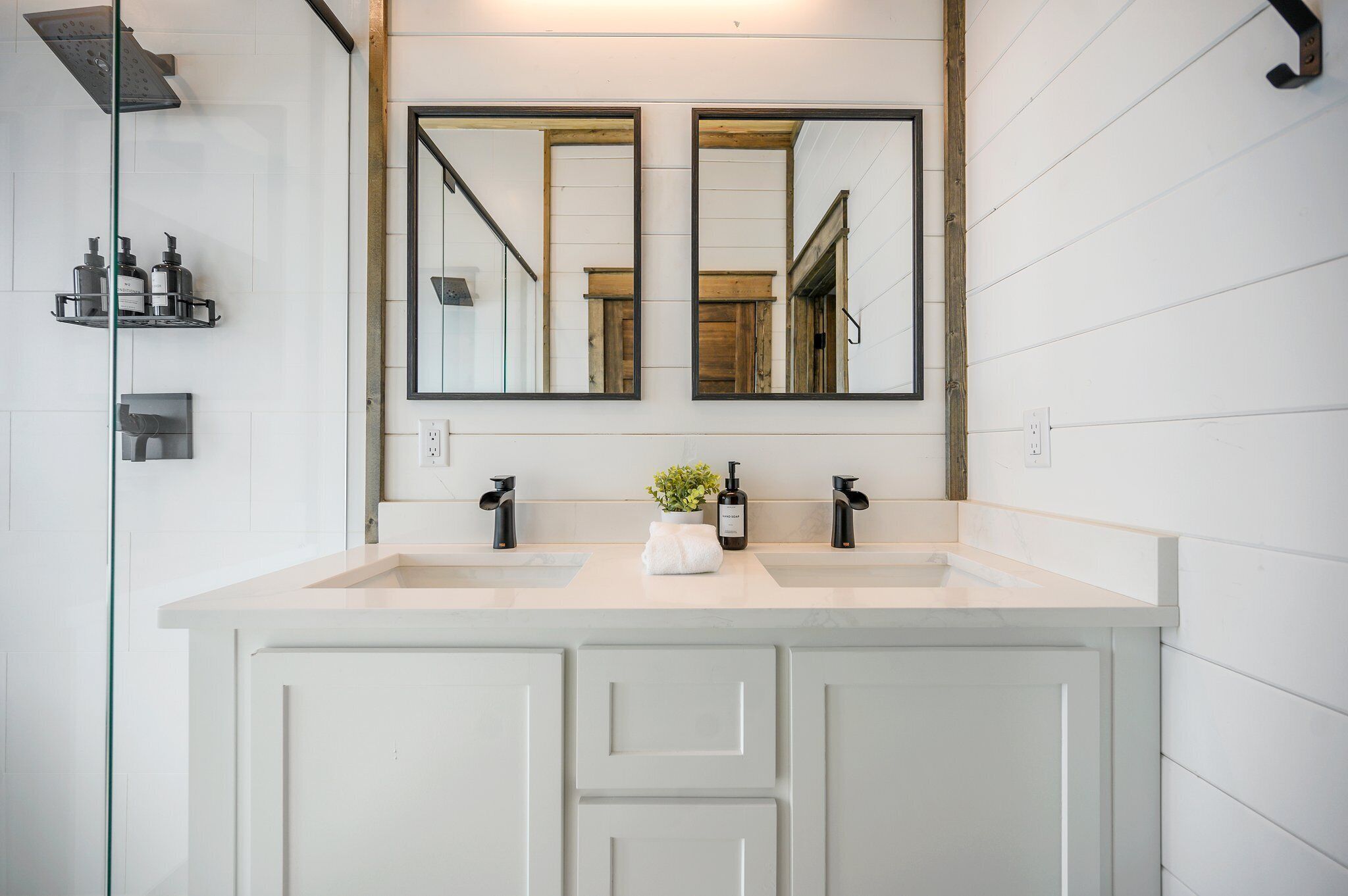 A bathroom with two sinks, a large mirror, and a shower.