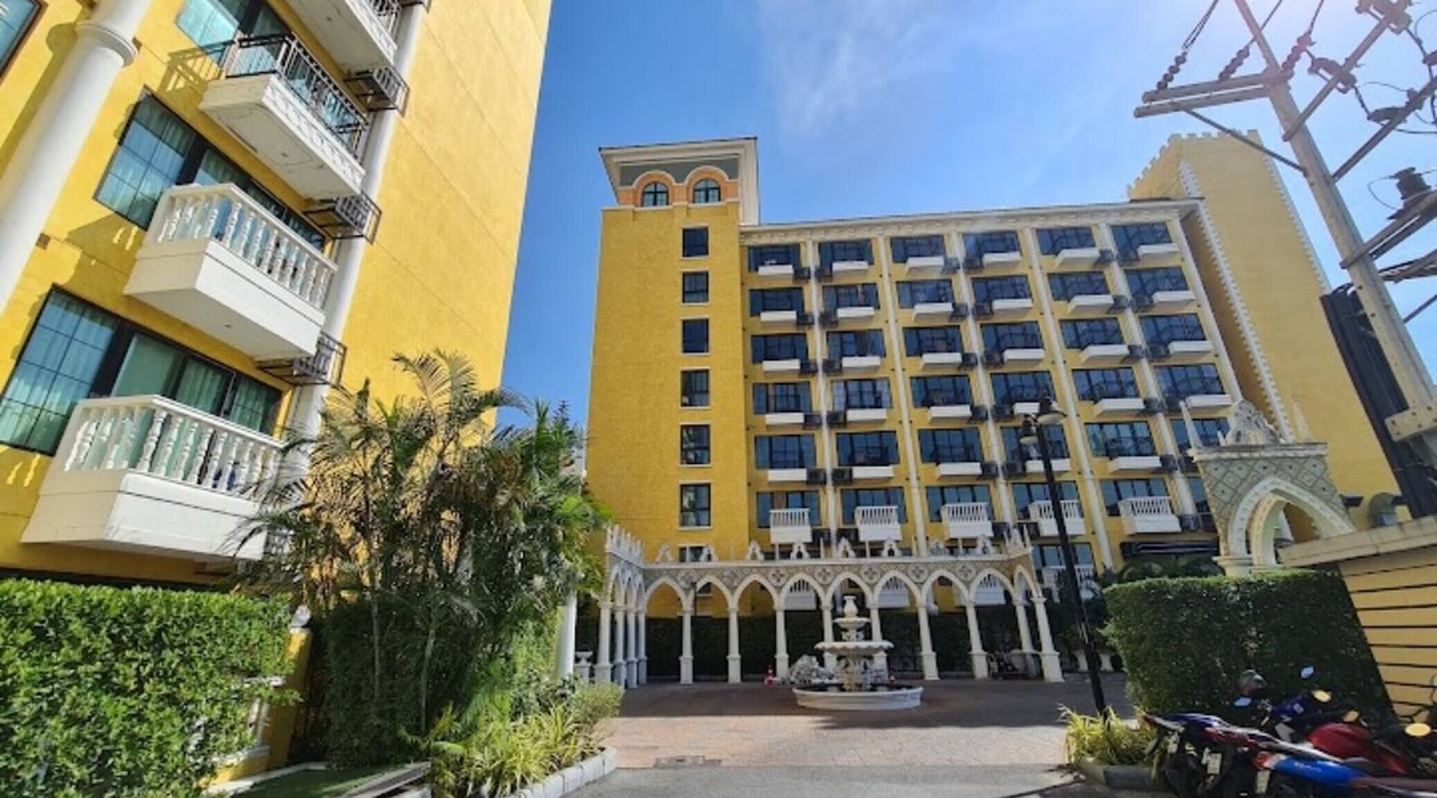A multi-story hotel with balconies, a central courtyard with a fountain, and a clear sky.