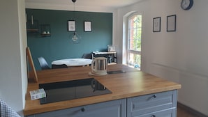 Eine moderne Küche mit einer Holz Arbeitsplatte, einem Wasserkocher und einer Kaffeemaschine. An den Wänden hängen gerahmte Bilder und ein Fenster bietet Blick auf Grünfläche.