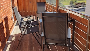 Eine Holzterrasse mit Metallgeländer, einer Ziegelwand und Blick auf eine grüne Landschaft.