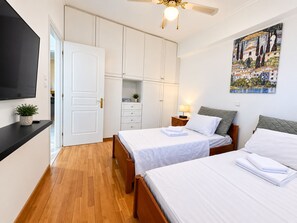 A hotel room with two beds, a flat-screen TV, a ceiling fan, and a painting on the wall. - Eagles Nest Villa Your Grecian Paradise (Kropia)