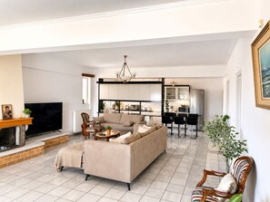 A modern living room with a sofa, chairs, a fireplace, and a kitchen area in the background. - Eagles Nest Villa Your Grecian Paradise (Kropia)