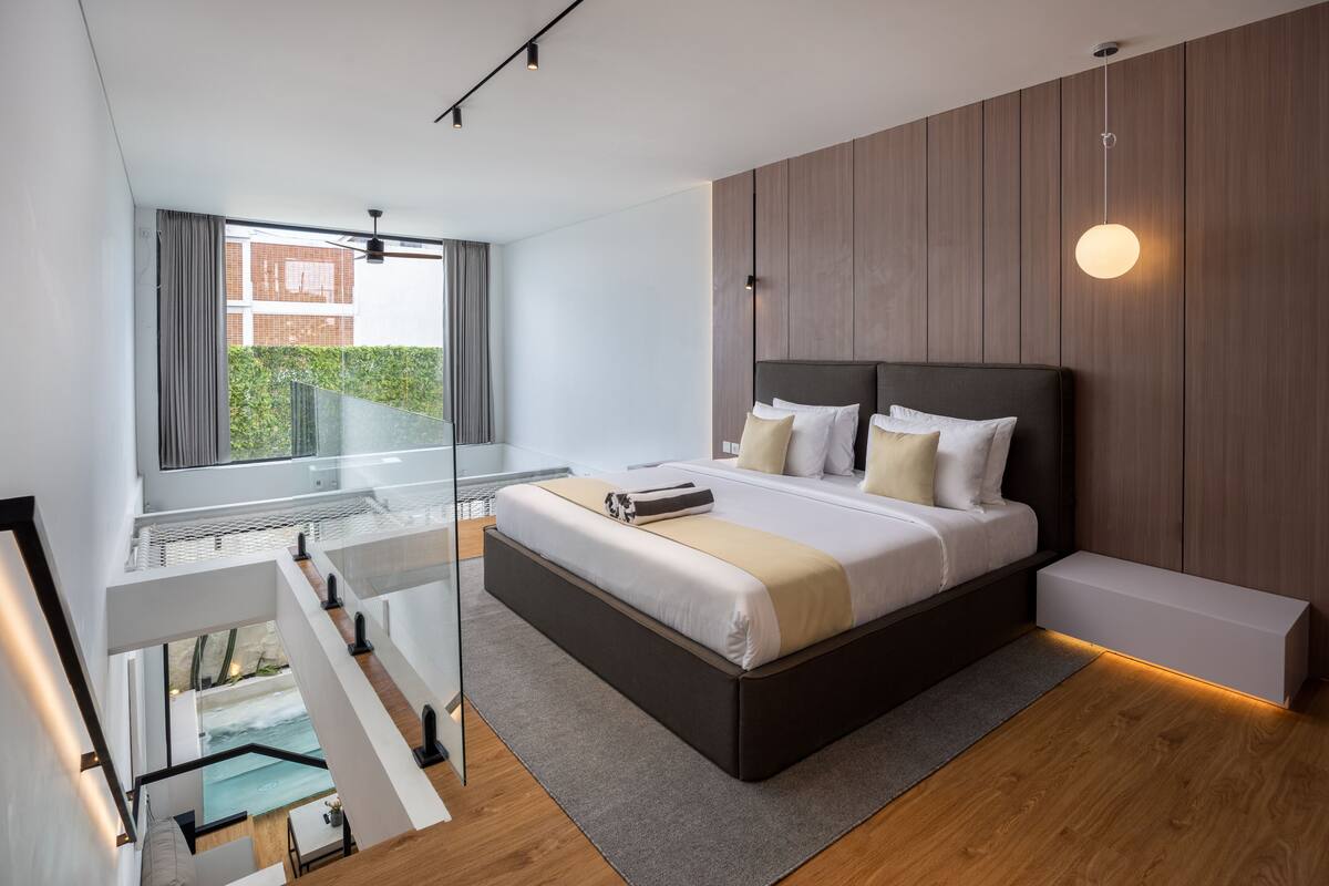 A modern bedroom with a large bed, a glass balcony, and a view of greenery.