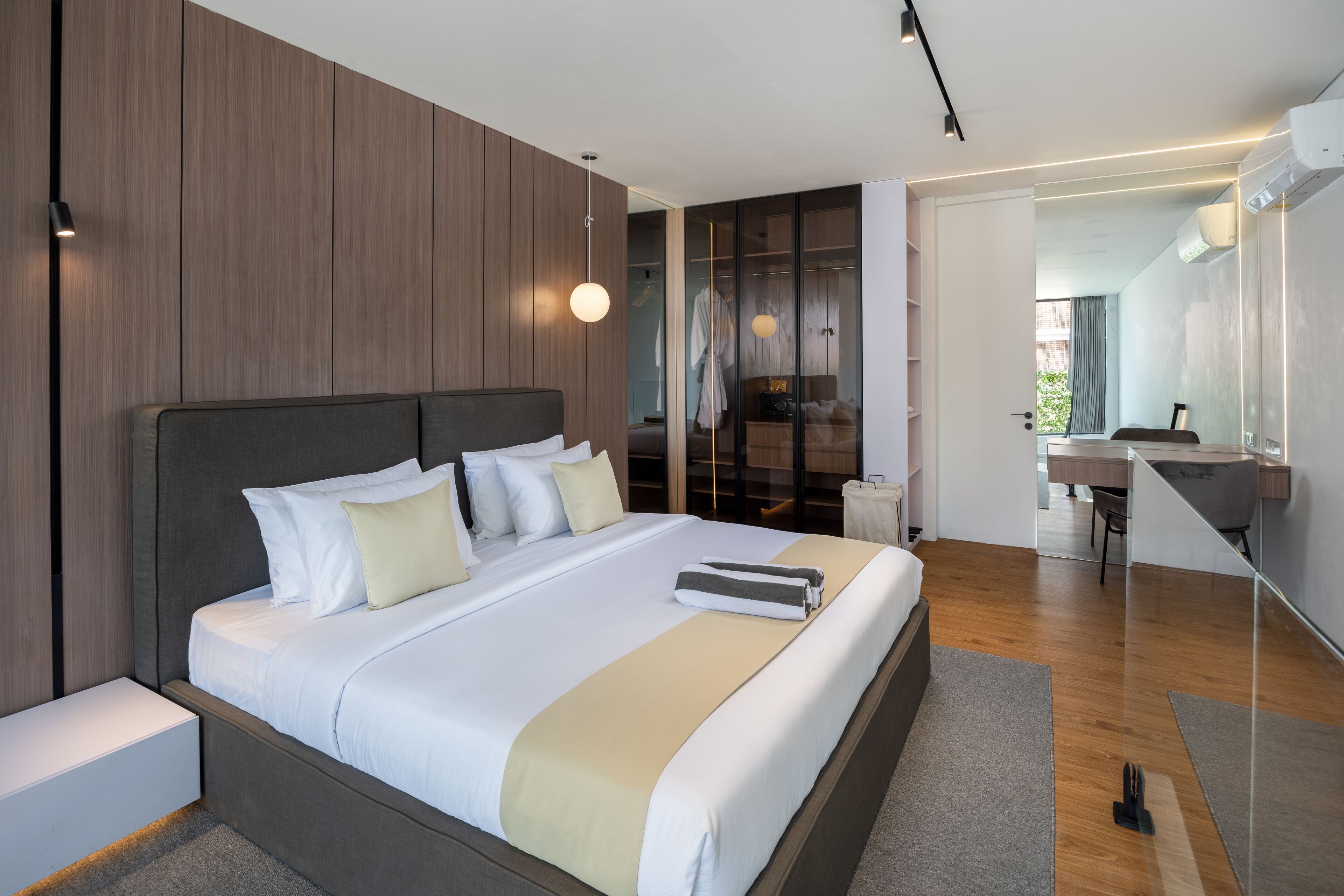 A modern bedroom with a large bed, bedside tables, a wardrobe, and a bathroom with a mirror and sink.