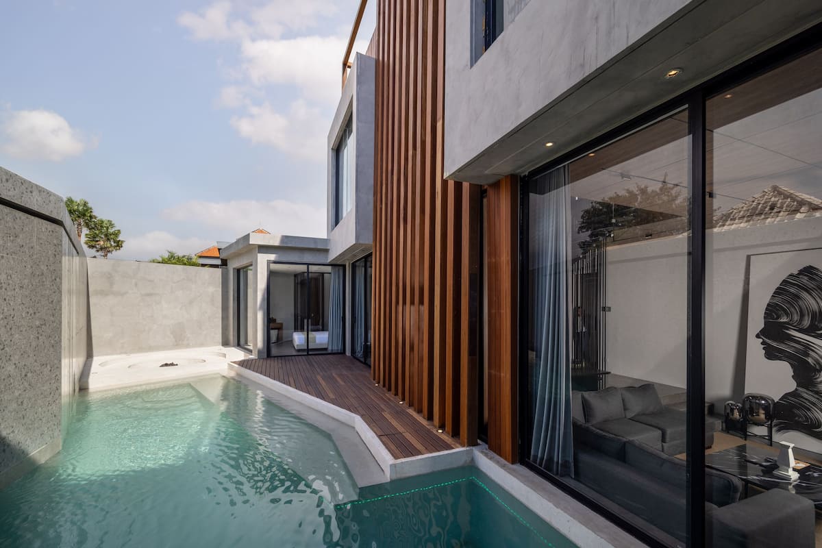 A modern house with a swimming pool, a wooden deck, and a large glass door leading to a living area.