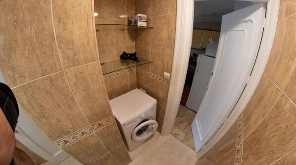 Une petite salle de bain équipée de toilettes, d’un lave-linge et d’étagères en verre.