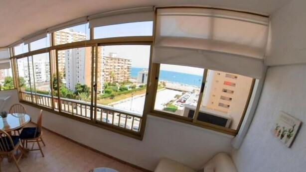 A balcony with a view of the sea and buildings, a round table with chairs, and a sofa with cushions. - Poseidón. Beachfront apartment (Fuengirola)