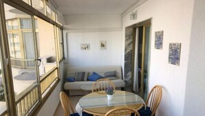 A balcony with a glass table and chairs, a sofa, and a view of a building. - Poseidón. Beachfront apartment (Fuengirola)