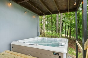 A hot tub with a control panel, surrounded by a wooden deck and a covered area with string lights.