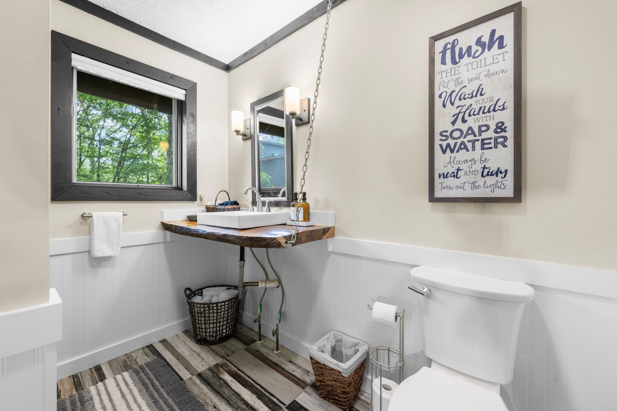 A bathroom with a window, a sink, a toilet, and a hanging light fixture.