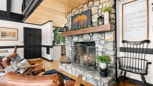 Un salon chaleureux avec une cheminée en pierre, des fauteuils en cuir et un livre d’histoires encadré accroché au mur.