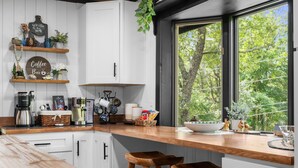 Une cuisine moderne avec des meubles blancs, un plan de travail en bois et une fenêtre donnant sur les arbres.