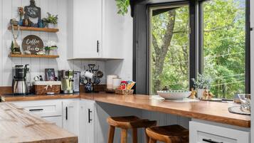 A modern kitchen with white cabinets, a wooden countertop, and a window with a view of trees.