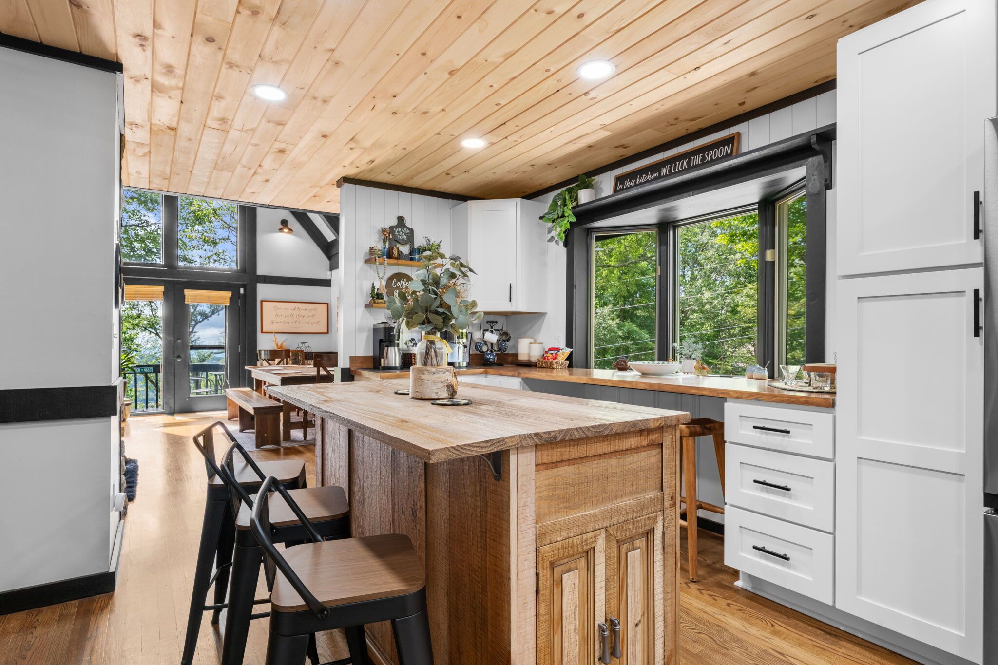 A modern kitchen with a wooden ceiling, white cabinets, and a large island with bar stools.