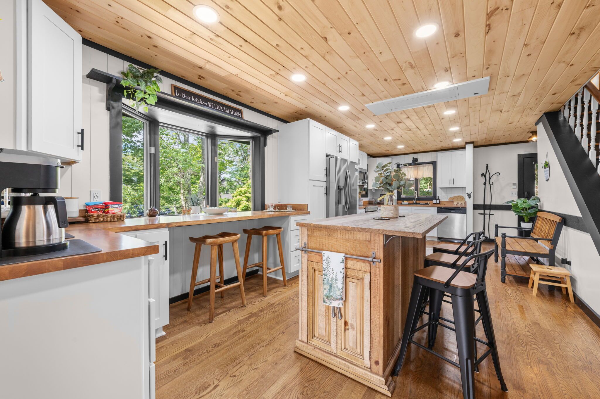 A modern kitchen with wooden flooring, white cabinets, and a large island with stools.
