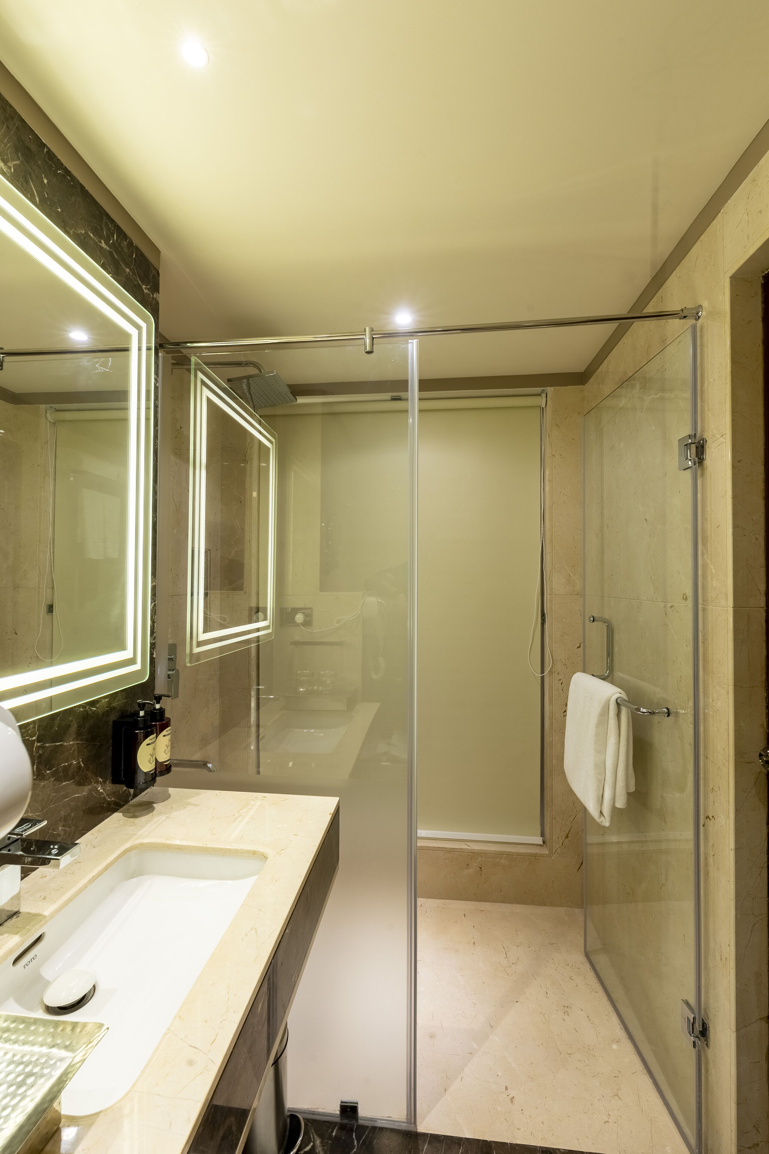 A modern bathroom with a glass-enclosed shower, a large mirror with LED lighting, and a marble countertop.