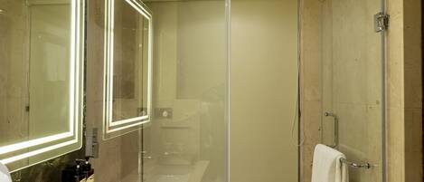 Un baño moderno con cabina de ducha de vidrio, un espejo grande con iluminación LED y encimera de mármol.