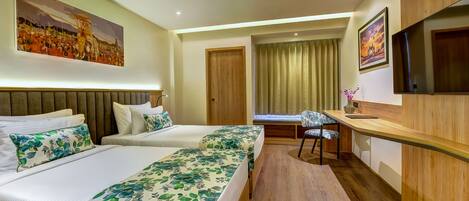 A hotel room with two beds, a desk, a chair, a TV, and artwork on the walls.