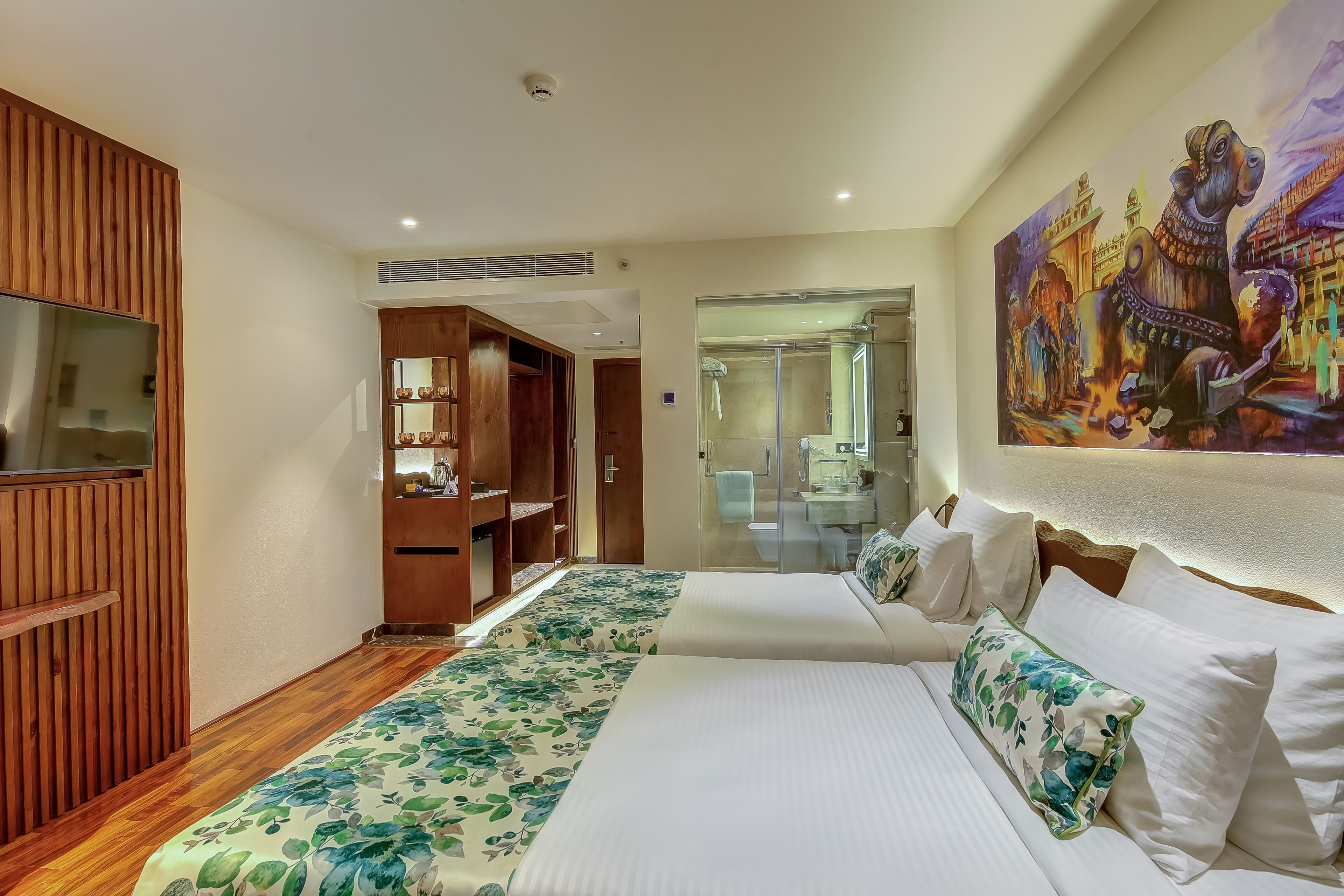 A hotel room with two beds, wooden paneling, a large painting, and a bathroom with a glass shower.