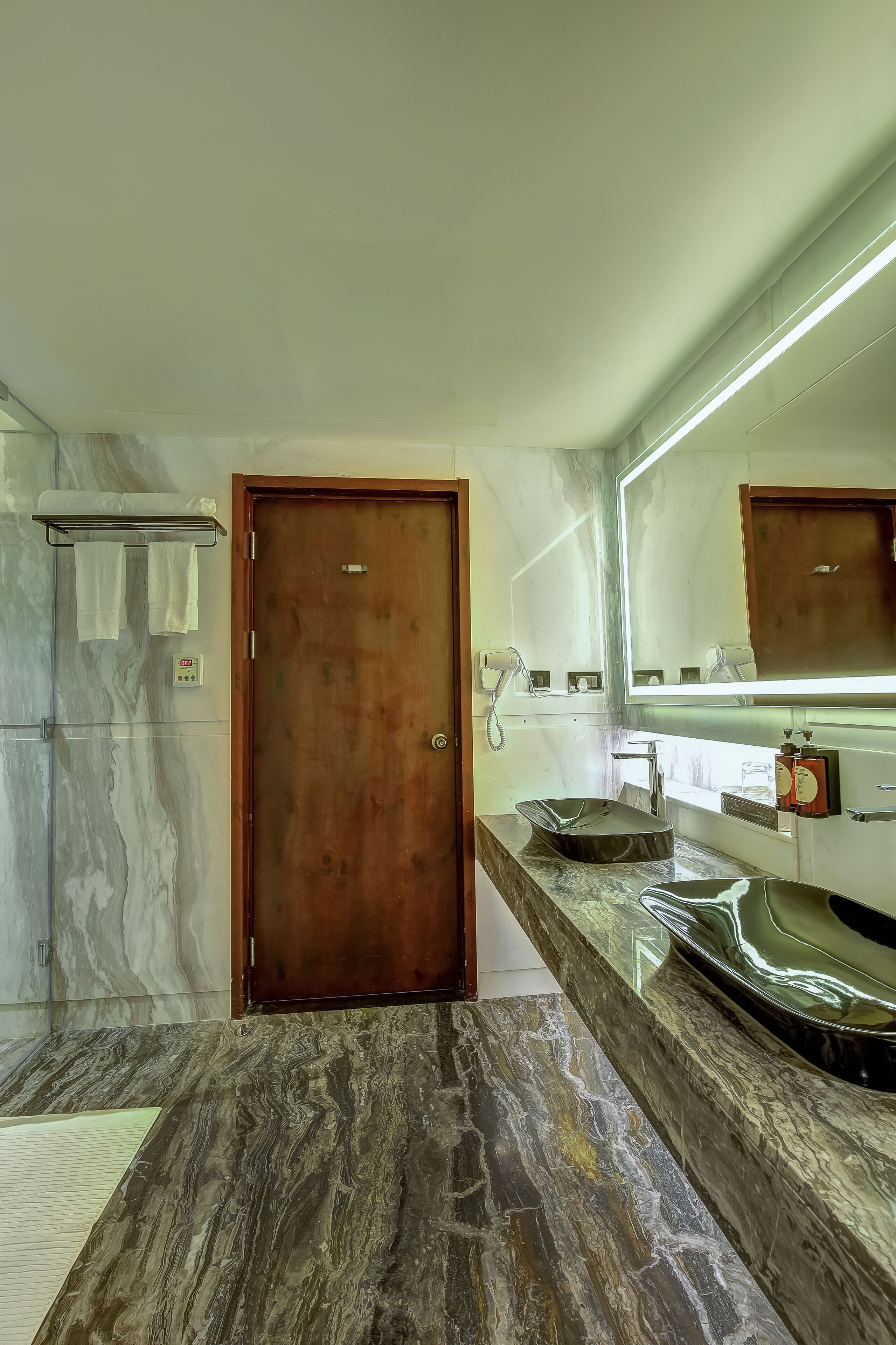 A bathroom with marble flooring, a wooden door, a sink with a mirror, and a towel rack.