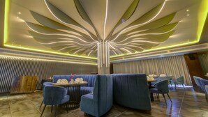 Interior de un restaurante moderno con una lámpara central, asientos azules y una pared con diseño.