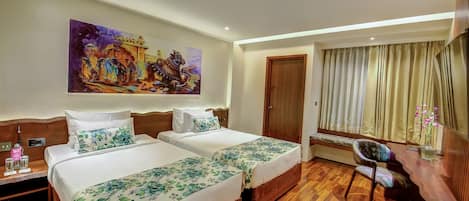 Habitación de hotel con dos camas, un escritorio de madera, una silla, un cuadro en la pared y una ventana con cortinas.