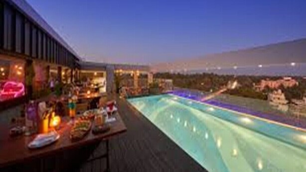 Un bar en la azotea con piscina, con vistas a un paisaje urbano al atardecer.