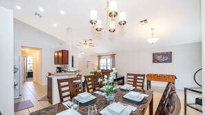 Ein Essbereich mit einem Marmortisch, gedeckt für vier Personen, umgeben von Holzstühlen. Eine Chandelüster hängt darüber, und ein Deckenventilator ist sichtbar.