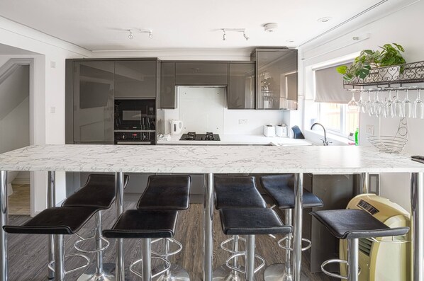 A modern kitchen with a marble countertop, black bar stools, and a built-in oven.