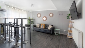 A modern living room with a grey sofa, a dining area with bar stools, and a mounted TV. - Get Away Home With Hot Tub Sleeps 7 (Peacehaven)
