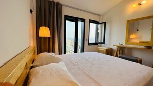 Ein Hotelzimmer mit einem großen Bett, einem Schreibtisch, einem Stuhl, einem Spiegel und Blick auf die Stadt.