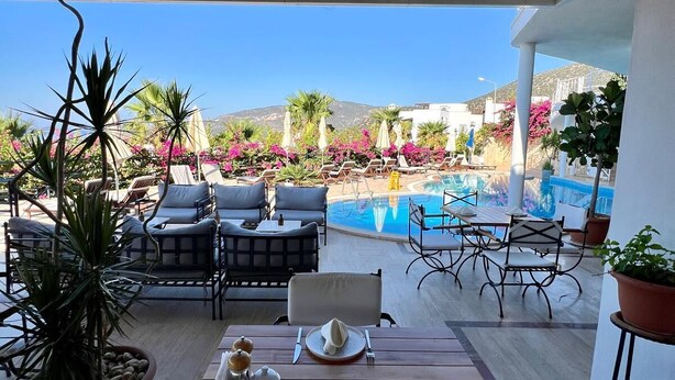 Eine Terrasse im Freien mit Holztischen und -stühlen, einem Pool und Kübelpflanzen.