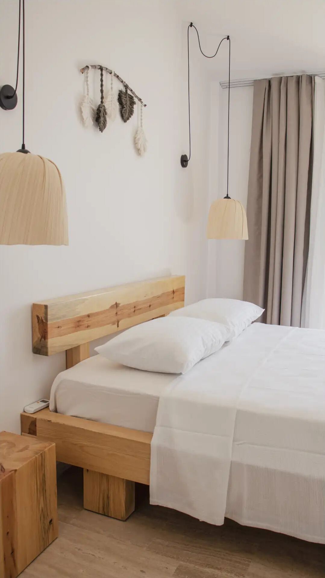 Quarto minimalista com estrutura de cama de madeira, roupa de cama branca e duas luminárias pendentes.