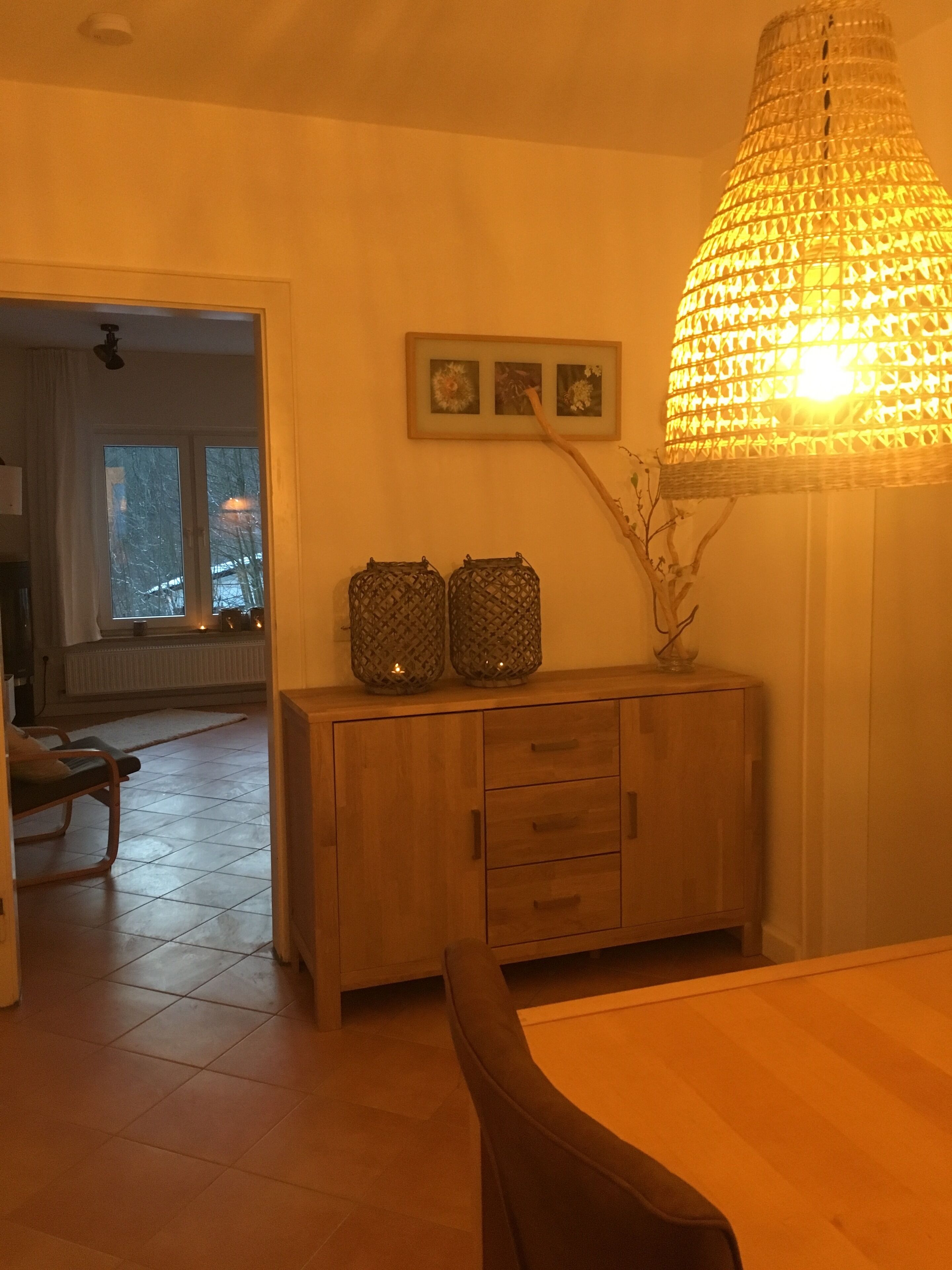 Una sala de estar con un aparador de madera, dos cestas decorativas, una lámpara colgante grande y un cuadro enmarcado en la pared.